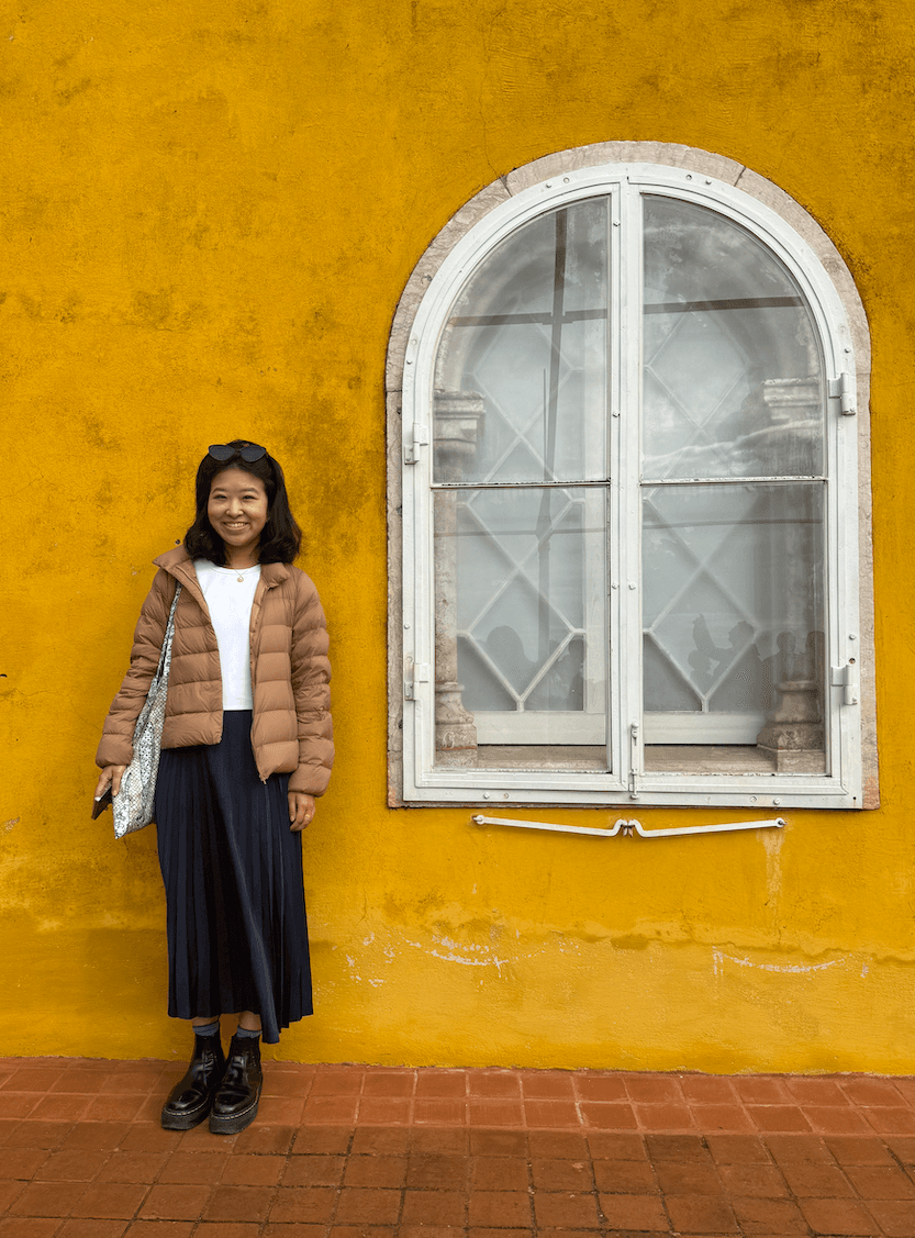 Melanie Chen standing against a yellow wall in Sintra, Portugal